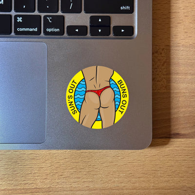 Suns Out Buns Out shimmer sticker with man in thong illustration showing on laptop